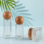 Clear glass skincare bottles and cream jars with natural wood closures on matching light cyan display platforms beneath visible green palm leaves