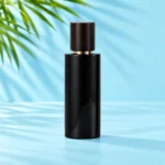 Tall glossy black glass lotion bottle with dark wood overcap and gold collar on a cyan tabletop with green palm leaves