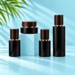 Three black glass bottles and a matching cream jar with dark wood closures arranged on cyan tabletop and cube with visible green palm leaves