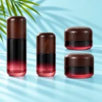 Burgundy gradient glass bottles and cream jars with dark rounded wood closures on a light cyan tabletop with visible green palm foliage