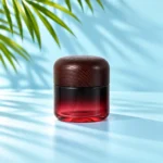 Tall burgundy gradient glass cream jar with a dark rounded wood lid on a light cyan tabletop with visible green palm foliage
