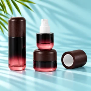 Burgundy gradient glass bottle with dark wood cap, exposed white pump and matching cream jar on a light cyan tabletop with visible green palm leaves