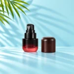 Burgundy gradient glass lotion bottle with exposed black pump beside its dark rounded wood cap on a light cyan tabletop beneath visible palm leaves