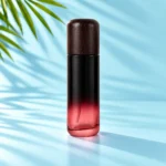 Tall burgundy gradient glass lotion bottle with a dark rounded wood cap and black pump option on a light cyan tabletop beside green palm leaves