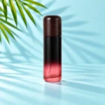 Tall burgundy gradient glass lotion bottle with a dark rounded wood cap and white pump option on a light cyan tabletop beside green palm leaves