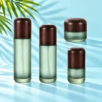 Frosted green glass skincare bottles and matching cream jars with dark rounded wood closures on matching light cyan steps beside green palm foliage