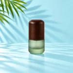 Close view of a small frosted green glass cream jar with a tall rounded dark wood lid on a light cyan tabletop with visible palm leaves