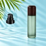 Frosted green glass lotion bottle with rounded dark wood cap and black pump detail inset on a light cyan scene with visible palm leaves