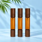 Three amber double ended glass perfume bottles with dark wood caps on both ends on a pale blue cyan tabletop