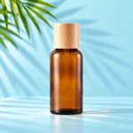 Tall amber glass essential oil bottle with a light natural wood cap on a mint tabletop against a matching cyan background with green palm leaves