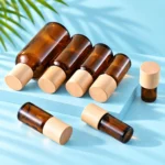 Seven amber glass essential oil bottles with natural wood caps arranged upright and lying on a cyan rectangular display platform and matching mint tabletop