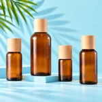 Four amber glass essential oil bottles with natural wood caps on a mint tabletop and matching cyan square platform with visible green palm foliage