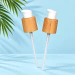 Two detached lotion pumps with bamboo collars, white heads and transparent dip tubes on a pale blue cyan background with green palm leaves