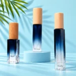 Three blue-to-clear gradient glass perfume bottles with light beech caps on matching mint platforms with green palm leaves