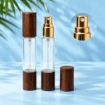 Two clear dual ended perfume bottles with wood caps and a magnified gold atomizer detail on a pale blue cyan background