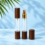 Two clear double ended glass perfume bottles with dark wood caps, one gold spray exposed and a detached cap alongside