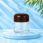 Tall clear glass cream jar with rounded dark wood lid on a cyan platform, nominal 100g version.