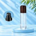Tall clear glass lotion bottle with rounded dark wood cap and framed black pump detail on a cyan background.