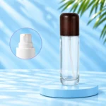 Tall clear glass lotion bottle with rounded dark wood cap and framed white pump detail on a cyan background.