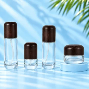 Three clear glass lotion bottles and one matching cream jar with rounded dark wood closures on a cyan tabletop and pedestal.