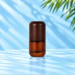 Compact amber glass lotion bottle with rounded dark wood cap on a cyan tabletop.