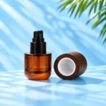 Open amber glass lotion bottle with black pump and detached dark wood cap resting on a cyan tabletop, white inner liner visible.