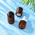 Overhead view of capped amber glass lotion bottle and open white pump bottle with detached wood cap on cyan tabletop.
