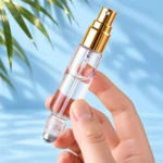 Hand holding a clear double ended perfume bottle with a gold spray atomizer and an exposed silver roller ball