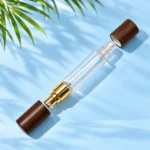 Clear dual ended glass perfume bottle with gold atomizer, roller ball and two detached dark wood caps