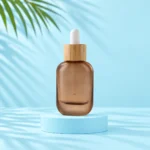 Flat rounded rectangular frosted brown glass dropper bottle with bamboo collar and white bulb on a pale blue cylinder.