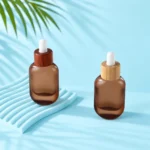 Two frosted brown glass dropper bottles with sapele and bamboo collars on a pale blue tabletop and matching curved support.