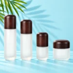 Three frosted glass lotion bottles and a matching cream jar with rounded wood closures on a mint tabletop