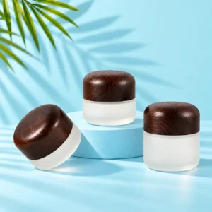 Three frosted glass cream jars with rounded dark wood lids on a mint tabletop and matching cyan display platform with green palm foliage