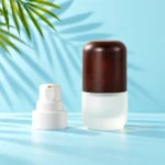 Compact frosted glass lotion bottle with a rounded dark wood cap beside a detached white pump on a mint tabletop