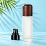 Tall frosted glass lotion bottle with a rounded dark wood cap beside a detached black pump in a mint palm studio