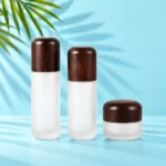 Two frosted glass lotion bottles and a matching cream jar with rounded dark wood closures in a mint palm studio