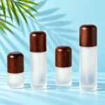 Four frosted glass lotion bottles with rounded dark wood caps on a mint tabletop with green palm leaves
