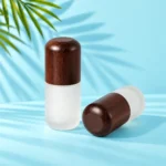 Two frosted glass lotion bottles with rounded dark wood caps, one upright and one lying on a mint tabletop