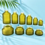 Six uncapped olive green glass bottles and four open cream jars showing threaded mouths on a pale blue cyan tabletop