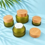 Four olive green glass cream jars with bamboo lids, including an open jar with a white inner seal disk