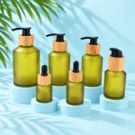 Six olive green frosted glass pump and dropper bottles with bamboo collars on a pale blue cyan tabletop