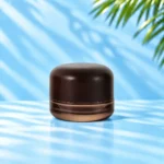 Compact smoke gray translucent glass cream jar in the 30g nominal size with a rounded dark wood lid on a cyan tabletop.
