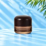 Smoke gray translucent glass cream jar in the 50g nominal size with a rounded dark wood lid on a cyan tabletop.