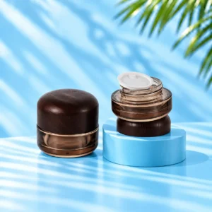 Two smoke gray glass cream jars with rounded wood lids, showing a closed jar and an open jar with white inner liner on a cyan platform.