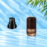 Compact smoke gray glass lotion bottle with rounded wood cap and a close-up inset of the black lotion pump.