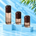 Three smoke gray glass lotion bottles with rounded dark wood caps displayed on cyan stepped platforms.