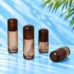 Three upright smoke gray glass lotion bottles and one horizontal bottle with rounded dark wood caps on a cyan tabletop.