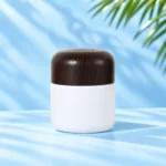 Tall opaque white cream jar with rounded dark solid wood lid on a pale blue cyan tabletop. Nominal 100g version.