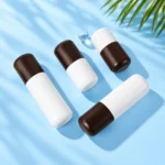 Four opaque white lotion bottles with rounded dark wood caps arranged diagonally on a cyan tabletop, viewed from above.